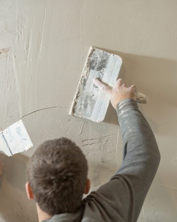 a man stands at a rough plastered wall with spatulas.