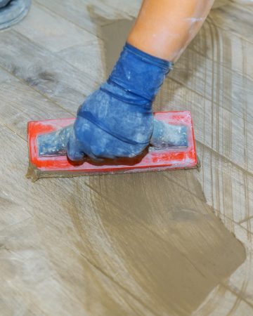 Hand of flooring on gray color of new grout tile on tile gray for the final step for flooring
